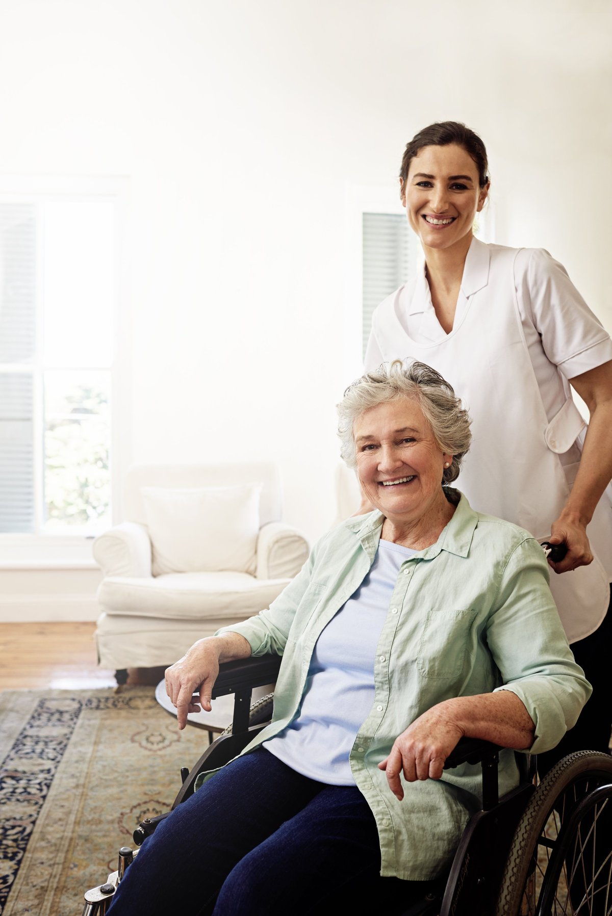 A smiling caregiver alongside a senior woman in a wheelchair at home